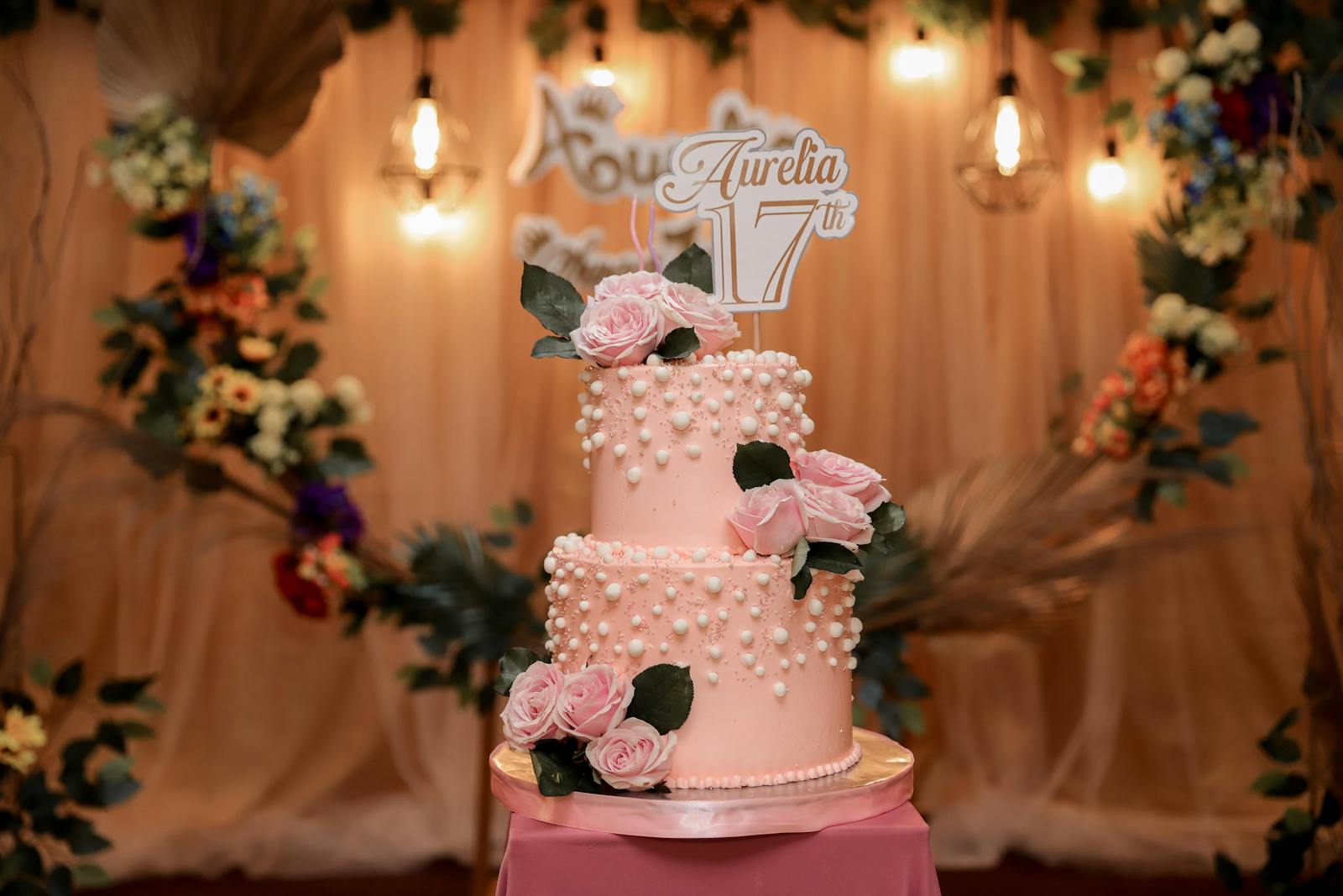 Beautiful pink two-tier birthday cake adorned with roses and pearls, perfect for celebrations.